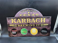 Vintage-style sign for Karbach Brewing Co. with brand names on a faux wood background